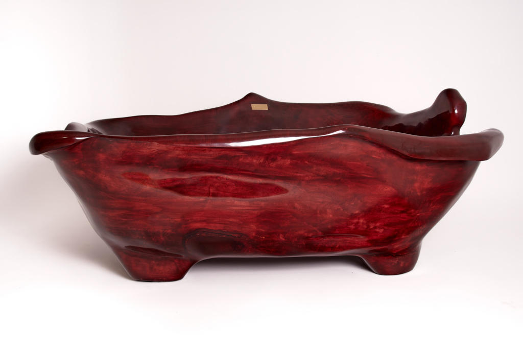 A Bathtub from Logniture in a Royal Red color, featuring an elegant polished finish and organic curves. Its unique sculptural design, carved from solid wood, highlights the natural wood grain beautifully.
